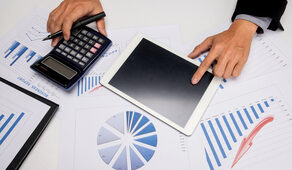 Visão aérea de profissional analisando gráficos financeiros com calculadora e tablet sobre a mesa.